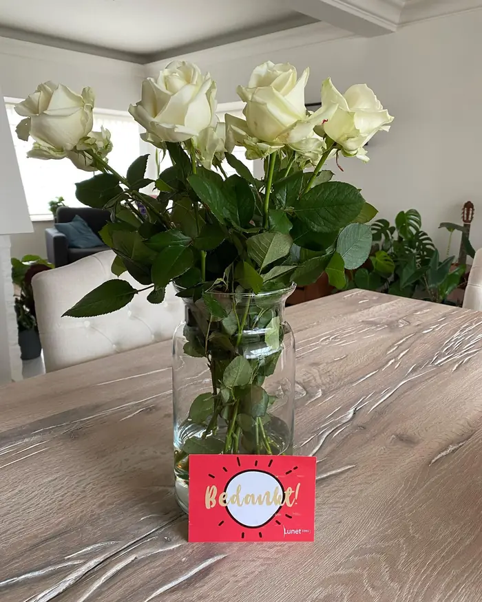 Witte rozen in een vaas met een rood kaartje waarop Bedankt staat