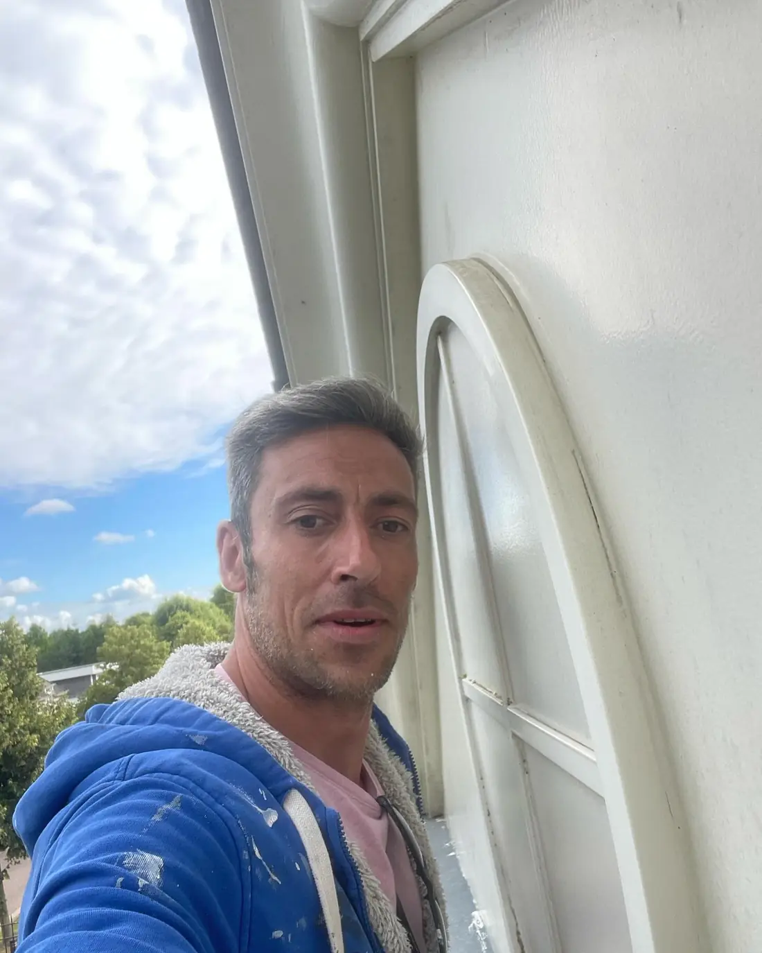 Dennis Leysen in een blauwe hoodie met verfspatten, aan een raam