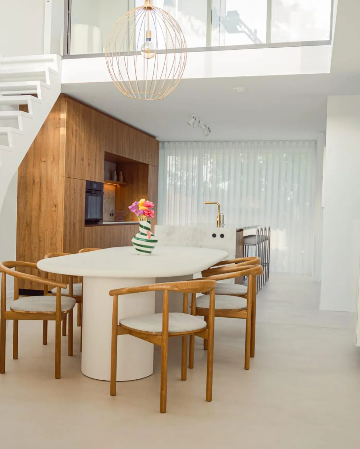 Lichte eetkamer met vide: witte muren en plafonds, een ronde witte tafel en houten stoelen