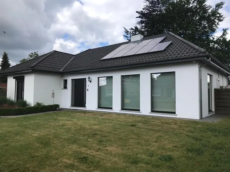 Gelijkvloerse woning met wit geschilderde gevel, zwart dak met zonnepanelen en een gazon