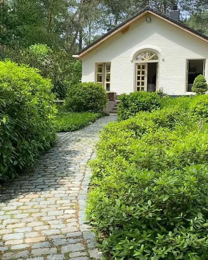 Wit geschilderd landelijk huisje met een kasseipad door de tuin